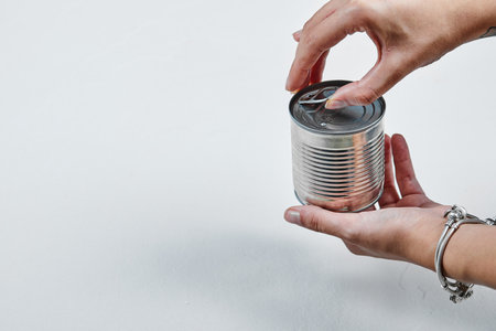 Hand holding a tin with boiled green peas on a white backgroundの写真素材
