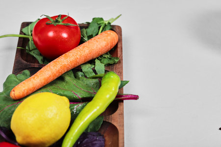 Peppers, greens, lemon, tomato and carrot on wooden plateの写真素材