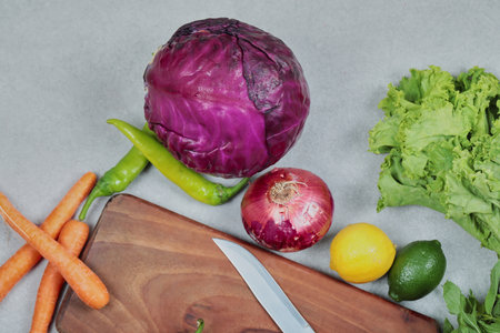 Fresh vegetables. Cabbage, onion, lemon, lime, greens on gray background with wooden board and knife