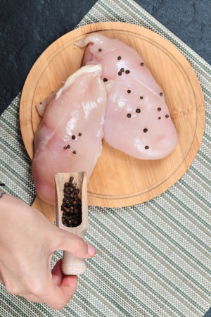 Raw chicken fillet on wooden board with greens and hand holding pepper grains spoonの写真素材