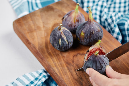 Hand cutting a fig on a wooden cutting board with a blue tableclothの写真素材