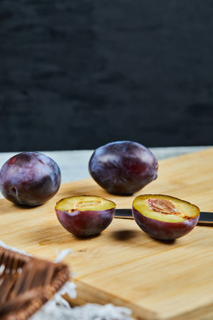 Ripe whole and half cut plums on wooden boardの写真素材