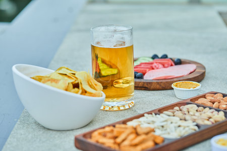 Assorted snacks, chips, a plate of sausages and a glass of beer on stone tableの写真素材