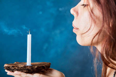 Young woman blowing out candle on blue backgroundの写真素材