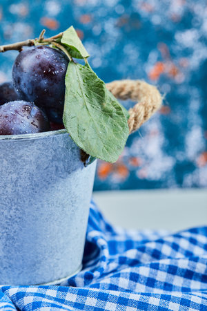Small bucket of fresh plums on a blue backgroundの写真素材