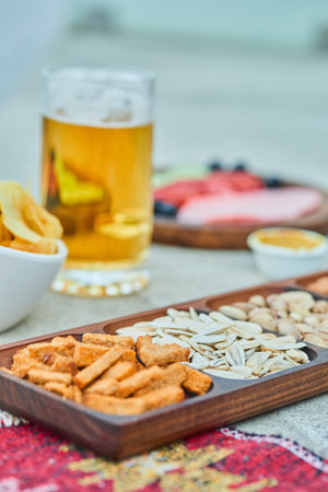 Assorted snacks, chips, a plate of sausages and a glass of beer on stone tableの写真素材