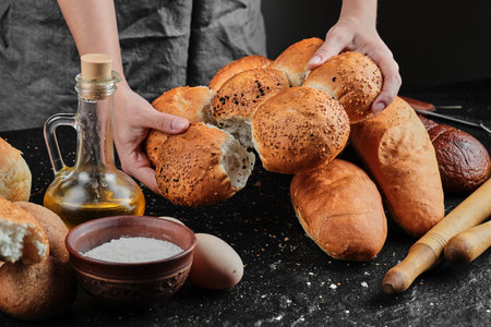 Woman holding bread on dark table with eggs, flour bowl and glass of oil