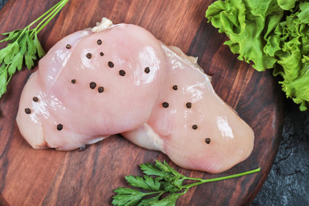 Wooden plate of raw chicken fillet with greens on dark tableの写真素材