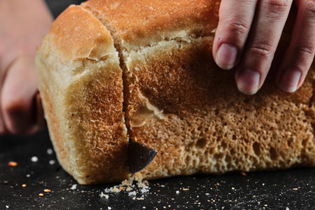 Woman cutting bread with knife on dark desk