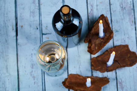 A glass of white wine and bottle on blue table with candles, top viewの写真素材