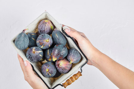 Hands holding a basket of purple figs on a white background