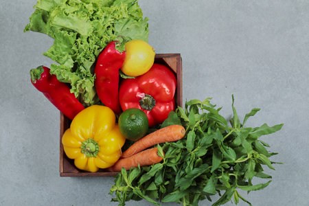 Wooden box of fresh peppers, carrots, lime, lemon, mint and lettuce on gray backgroundの写真素材