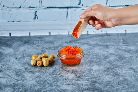 Woman hand taking a spoon of red caviar with olives on marble tableの写真素材