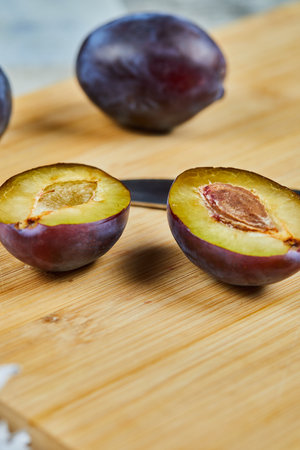 Whole and half cuts of plum on wooden boardの写真素材