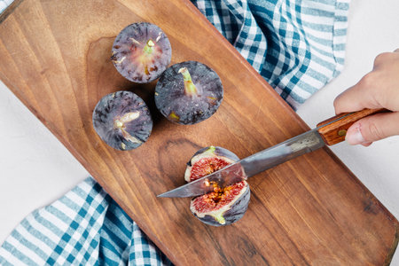 Hand cutting a fig on a wooden cutting board with a blue tablecloth