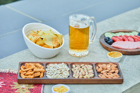 Assorted snacks, chips, a plate of sausages and a glass of beer on stone tableの写真素材