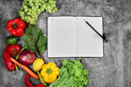Grapes, peppers, greens, lemon, tomato and empty notebook on marble backgroundの写真素材