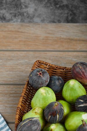 Green and black figs in a basket on a wooden tableの写真素材