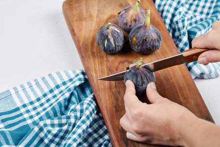 Hand cutting a fig on a wooden cutting board with a blue tableclothの写真素材
