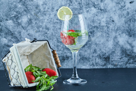 A glass of juice with whole fruits inside and basket of strawberries on blue backgroundの写真素材