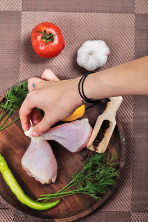 Hand holding raw chicken leg on wooden plate with fresh vegetablesの写真素材