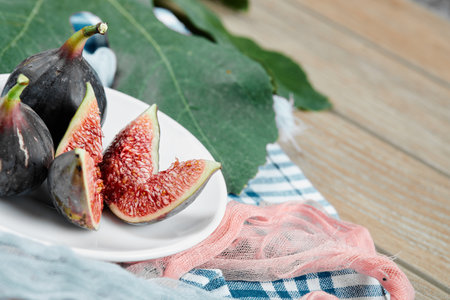A plate of whole and sliced black figs with blue and pink tablecloths on a wooden tableの写真素材