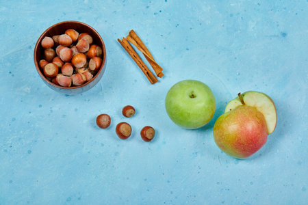 Apples, cinnamon and bowl of hazelnuts on blue backgroundの写真素材