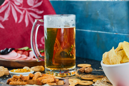 Assorted snacks, chips, a plate of sausages and a glass of beer on dark backgroundの写真素材
