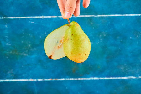 Holding half cut of ripe pear on blue backgroundの写真素材