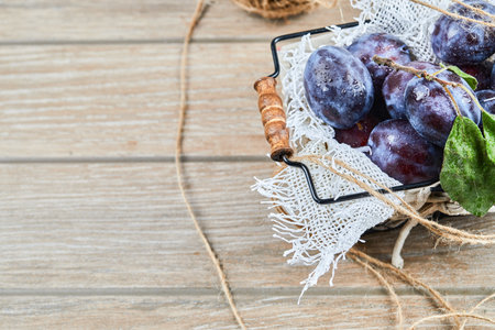 Garden plums in a basket on a wooden tableの写真素材