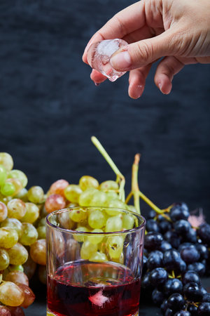 Bunch of grapes and a glass of juice with ice on dark backgroundの写真素材