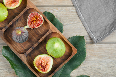 Whole and slices of green and black figs on a wooden platter with a leaf and a tableclothの写真素材