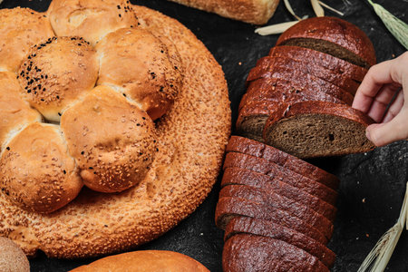 Woman taking slice of black bread on dark desk with various breadの写真素材