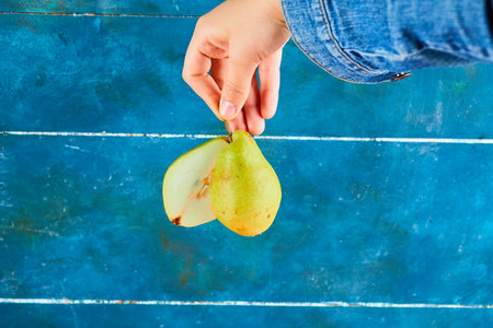 Holding half cut of ripe pear on blue background. High quality photoの写真素材