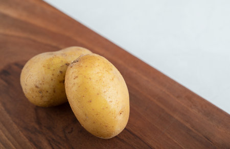 Close up photo of two fresh potatoes on brown wooden boardの写真素材