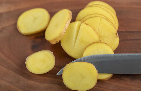 Sliced potato and knife on brown wooden board