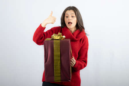 A young woman holding gift box and showing a thumb upの写真素材