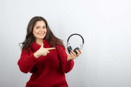 Photo of a young woman in red sweater pointing at headphonesの写真素材