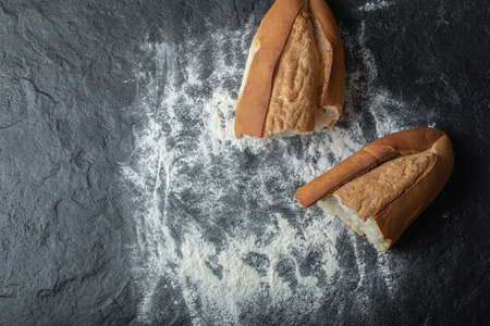 Two fresh bread pieces on flour on blackboard