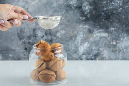 Female hand sprinkling a sugar powder on a walnut shaped cookiesの写真素材