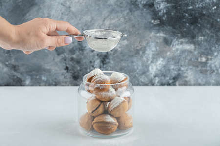 Female hand sprinkling a sugar powder on a walnut shaped cookiesの写真素材