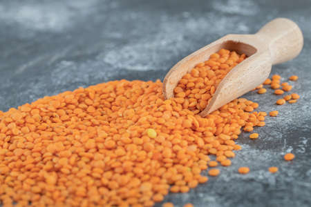 A wooden spoon full of raw lentils on a gray backgroundの写真素材