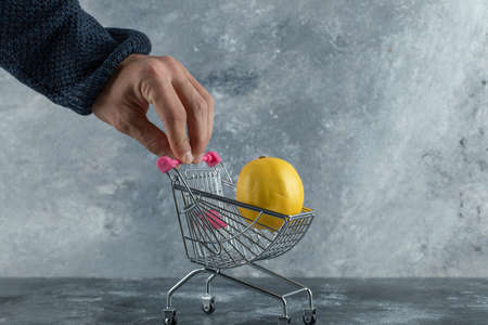 Male hand holding shopping cart with lemonの写真素材
