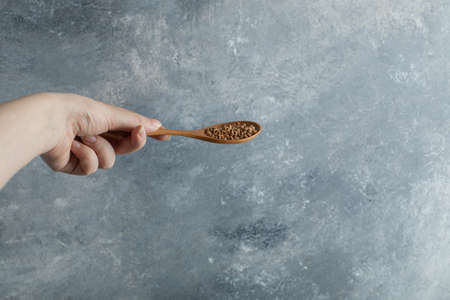Female hand holding wooden spoon of raw buckwheatの写真素材