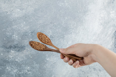 Female hand holding wooden spoons of raw buckwheatの写真素材