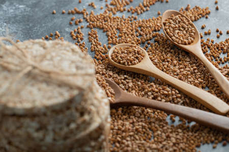 Spoons of raw buckwheat and delicious crispbread on marble surfaceの写真素材