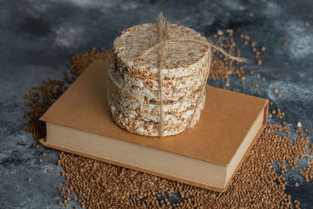 Yummy crispbread, uncooked buckwheat and book on marble surfaceの写真素材