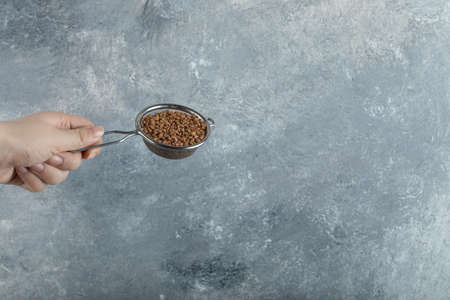 Female hand filtering raw buckwheat with strainer