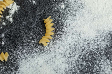 Raw spiral macaroni with flour on a dark background