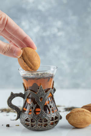 Female hand dipping a sweet walnut shaped cookie in cup of teaの写真素材